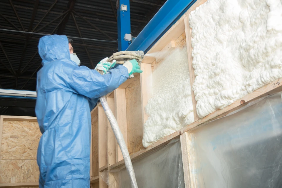 Ouvrier en combinaison de protection bleue appliquant de l'isolant par projection dans une structure en bois