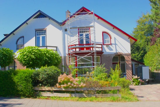 Scène extérieure montrant une maison résidentielle avec échafaudage métallique installé en façade pour travaux de rénovation