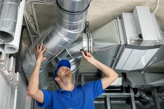Un technicien en tenue de travail bleue installe des conduits de ventilation dans un local technique